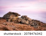Above a sea of clouds on top of Mount Brocken in the Harz mountains, Harz National Park, Saxony-Anhalt, Germany. Pink sunset sky and rock formations in autumn. Brocken Teufelskanzel, Hexenaltar.