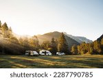 Camper vans in a valley with amazing landscape views of forest, mountains and sun rays during sunrise. Van road trip holiday and outdoor summer adventure. Nomad lifestyle concept