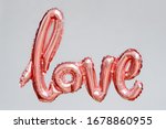 Love word from pink inflatable balloon floating in the air on grey background. The concept of romance, Valentine's Day. Love rose gold foil balloon