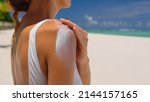 Small photo of Close up of a happy smiling young woman is applying a sunscreen or sun tanning lotion on a shoulder to take care of her skin on a seaside beach during holidays vacation.