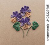 Small photo of quilling card with violet flowers on brown paper background. Spring flowers. Hand made of greeting cards in paper quilling technique. Handicraft at home. Hobby, home office.