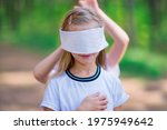 Small photo of The girl is blindfolded for playing blind man's buffoonery outdoors in the forest.