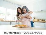 Small photo of Asian lovely family, young daughter look to old mother cook in kitchen. Beautiful female enjoy spend leisure time and hugging senior elderly mom bake croissant on table in house. Activity relationship