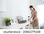 Small photo of Asian cleaning service woman worker cleaning in living room at home. Beautiful young girl housekeeper cleaner feel happy and use feather duster wiping messy dirty for housekeeping housework or chores