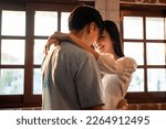 Asian young man and woman hugging each other in living room at home. Attractive romantic new marriage couple male and female spending time celebrate anniversary and valentine's day together in house.