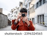 Asian backpacker use camera taking a picture of beautiful landscape. Young male tourist traveler travel alone on street in city, using cellphone record vlog on holiday vacation trip in Switzerland.
