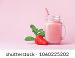 Strawberry smoothie or milkshake in mason jar decorated mint on pink table. Healthy food for breakfast and snack.