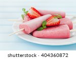Homemade strawberry ice cream or popsicles in plate on blue wooden table, frozen fruit juice, selective focus.