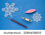Small photo of White snowflakes, woven using the technique of tatting lace, pink and yellow shuttles with threads and a crochet hook on a blue background. Needlework.