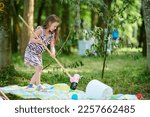 Small photo of Svetlogorsk, Russia - 13.08.2022 - Young girl plays croquet with croquet mallet and balls in outdoor forest children party, carefree childhood of cute attractive girl. Young lady in dress