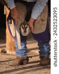 Small photo of Close up of blacksmith or farrier working on horse hoof with rasp rasping or filing outside of hoof trimming horse foot vertical image room for type male farrier wearing chaps or chinks cowboy boots