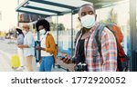 Small photo of Mixed-races young males and females people im medical masks standing in line at bus stop. Keeping safe social distance. African American stylish man tourist outdoor waiting for transport. Tourists.