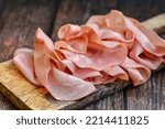 Small photo of Slices Of Traditional Italian antipasti mortadella Bolognese on a wooden cutting board.