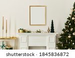 Christmas composition with gold mock up poster frame, white chimney and decoration. Christmas trees and wreath, candles, stars, light and elegant accessories. Template.