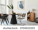 Stylish composition of dining room interior with design table, modern chairs, decoration, tropical leaf in vase, fruits, bookcase, abstract mock up paintings and elegant accessories in home decor.