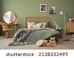 Small photo of Stylish bedroom interior design with mock up poster frames, bed, side table, rattan commode, vanity table and creative home accessories. Sage green wall. Template. Copy space.