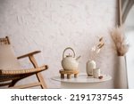 Boho and cozy interior of living room with rattan armchair, stylish coffee table, tea pot, vase with dried flowers, decoration and elegant accessories. Minimalist home decor. Template. 
