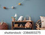 Small photo of Interior design of warm kids room interior with wooden sideboard, plush toys, pillow, pink basket, colorful garland, wooden camera, abacus and personal accessories. Home decor. Template.