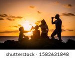 Friends toasting with bottles of beer, beautiful sunset on the ocean in background. Modern family cheering with drinks, amazing orange sky with clouds over the sea. Group of people enjoying together