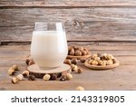 Small photo of Vegan non diary hazelnut milk in glass with whole hazelnuts on a linen napkin on a rustic wooden background. Lactose free hazelnut drink is plant based alternative milk. Healthy milk product, close up