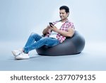 Small photo of Indian latin Man sitting on bean bag and using phone, Man relaxing on Bean bag on isolated Background