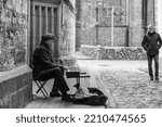 Small photo of Central District, Riga, LV-1050, Latvia October 2nd 2022 A male busker playing a keyboard on the doorstep of an old church in Riga Old Town as a man walks past. Black and white