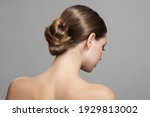 Woman with bun hairstyle on gray background. Bare back, shoulders and neck. Back view