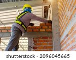 Small photo of Builder carefully puts red brick on the masonry. Quick work bricklayer. Guy measures level masonry. Man is building brick wall. Correctly calculate material. Builder manually carries brick structure,B