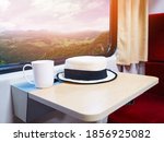 Close up white hat and cup of coffee on small folding table nearby glass window in the train with mountain landscape view. Happy holiday vacation concept.