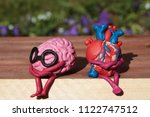 Small photo of Plasticine human heart and brain are sitting on a wooden bench in the park. Disharmonious unhappy person concept