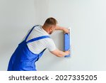 Small photo of Plasterer smoothes the wall surface with a wall grinder. Master builder grind a white plaster wall. a man in overalls grinds the surface in a respirator. experienced repairman