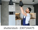 Small photo of Male electrician changes the light bulbs in the lamp. A young man in overalls performs technical work on electrification of premises