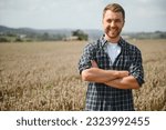 Small photo of Happy farmer proudly standing in a field. Combine harvester driver going to crop rich wheat harvest. Agronomist wearing flannel shirt, looking at camera on a farmland.
