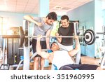 Small photo of Sportive man lifting weight in a gym - Coach inciting a body builder to finish his work out - Three friends working out in a weights room