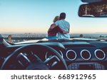 Couple watching sunset from popular view point in Los Angeles, California. Sitting on the sport convertible car hood