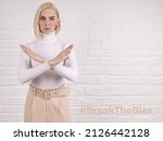 Small photo of Break the bias symbol of woman's international day. The arms of a girl in white are crossed on a white brick wall. Woman arms crossed to show solidarity, breaking stereotypes, inequality