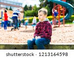 Small photo of A handsome boy with ADHD, Autism, Asperger Syndrome sitting at the park, scared and apprehensive about playing with the other children, looking nervous and worried