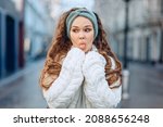 Small photo of Fooling around on camera. A young funny girl in a white knitted suit and a blue headband poses droll on the street. Eyes averted and tongue protruding. Blurry background. The concept of silly photos.