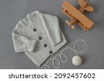 knitted children's cardigan with a ball of natural yarn on a gray background with a wooden toy in retro style, baby  layout