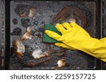 washing a dirty  baking sheet after cooking greasy food, a hand in a yellow rubber glove washes dirty dishes