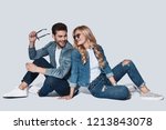 Looking perfect. Beautiful young couple in denim wear bonding and smiling while sitting against grey background