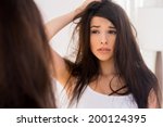 Good morning? Frustrated young woman looking at her reflection in the mirror and holding hand in hair