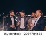 Group of handsome young men in suits and bowties drinking whiskey and smiling