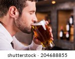Man drinking beer. Side view of handsome young man drinking beer while sitting at the bar counter 