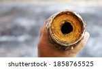 Small photo of Man's hand holds a clogged metal pipe. Old water pipes had rusty slag and clogged dirt inside the pipe. On the background of a cement floor with a copy area. Close focus and select an object