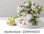 Beautiful composition with delicious French macarons and spring flowers in a white cup. Sweet dessert, early spring white and pink flowers, wedding decor, bride morning. Greeting card