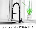 Black kitchen faucet on the silver sink near the glass of water 