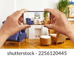 Augmented or mixed reality concept: hands holding smart phone with AR interior decoration app, visualizing the living room with an added poster print.