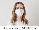Portrait of a young girl in a medical mask isolated on a white wall background. Young woman patient, copy space