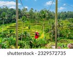 Young female tourist in red dress enjoying the Bali swing at tegalalang rice terrace in Bali, Indonesia
